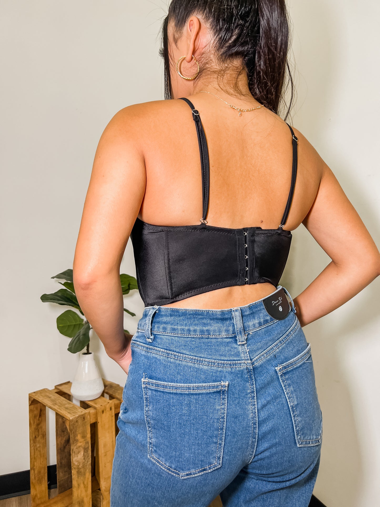 Model is turned away from camera. The back of the top is being presented to show the hook and eye closure at the back of the top. The top also shows adjustable straps.