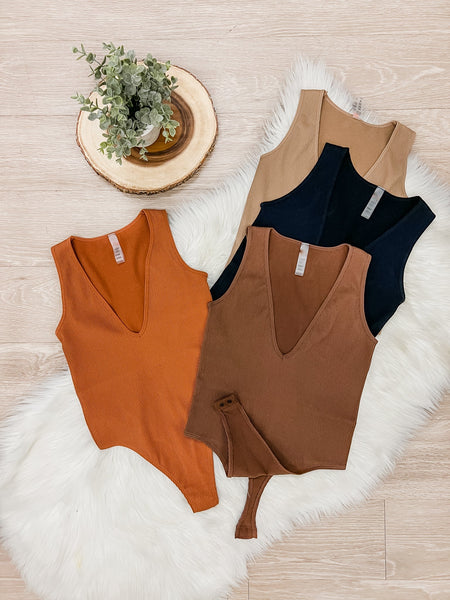 4 different color bodysuits placed on white rug. Colors shown are orange tan, black and brown.