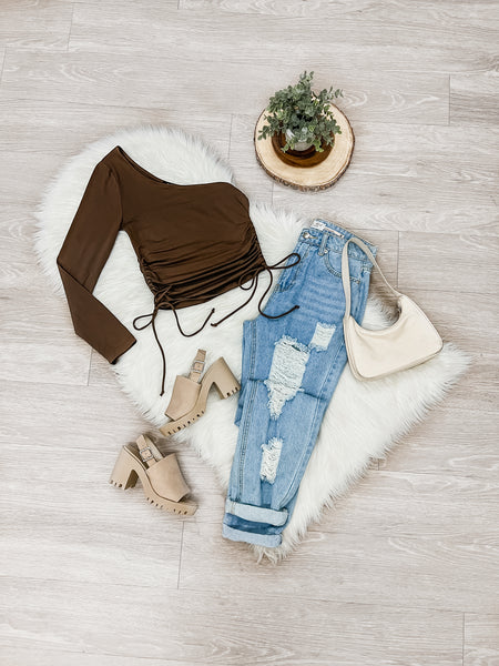 picture of long sleeve brown top with folded blue jeans next to pair of brown heels and white small purse laid out on floor