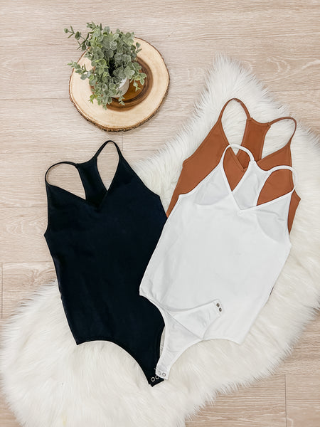 Flat lay image of 3 colored bodysuits. Black on the left and brown and white on the right side.