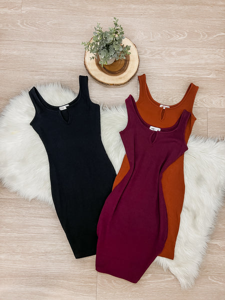 3 dresses in colors black, wine, and rust orange laid flat on white fur rug