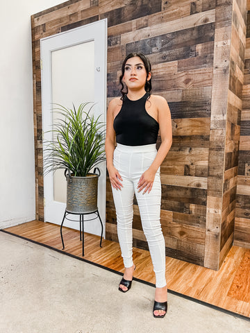 woman wearing black sleeveless top with white pants standing in front of wooden wall